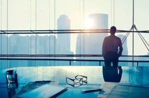 Business professional overlooking city skyline from modern office window.