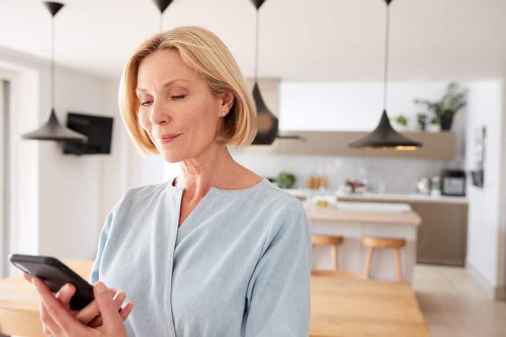 Injured woman reading message on her phone in modern kitchen.