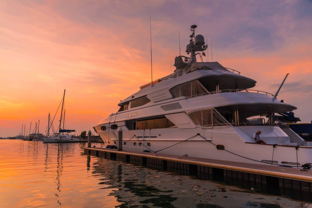 Luxury yacht docked at sunset with calm waters and vibrant sky.