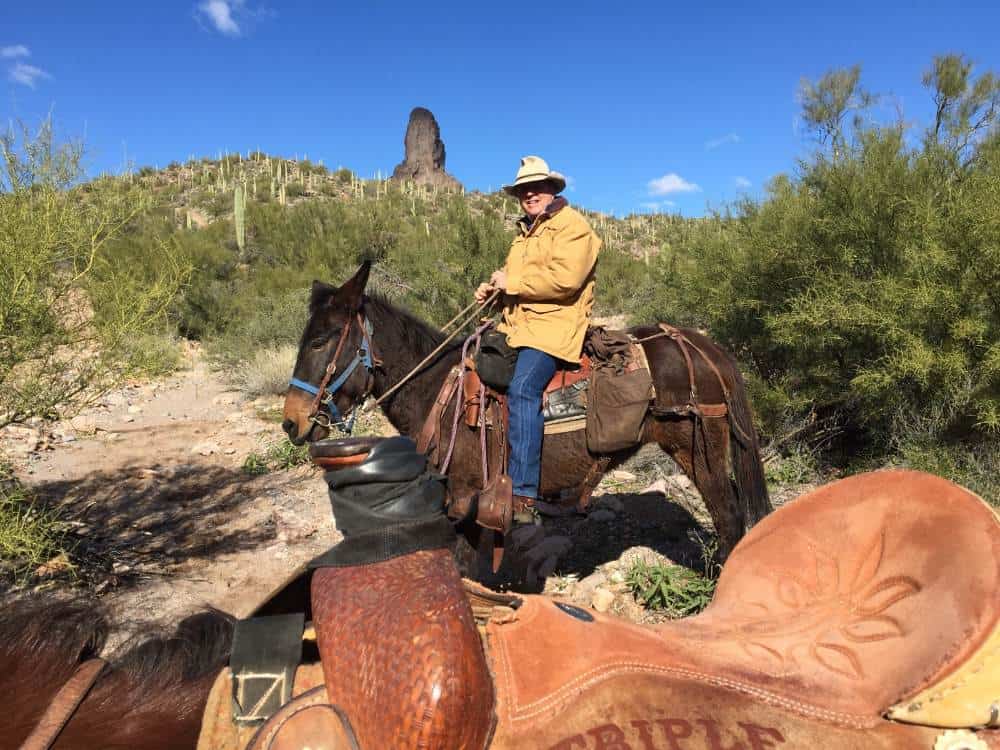 Matt Dana riding a horse in desert landscape with cacti and rock formations.