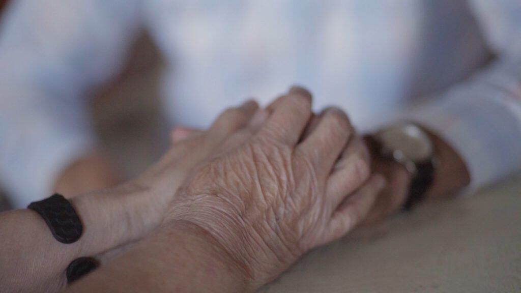 Elderly hand holding caregiver’s hand, support and compassion in senior care.