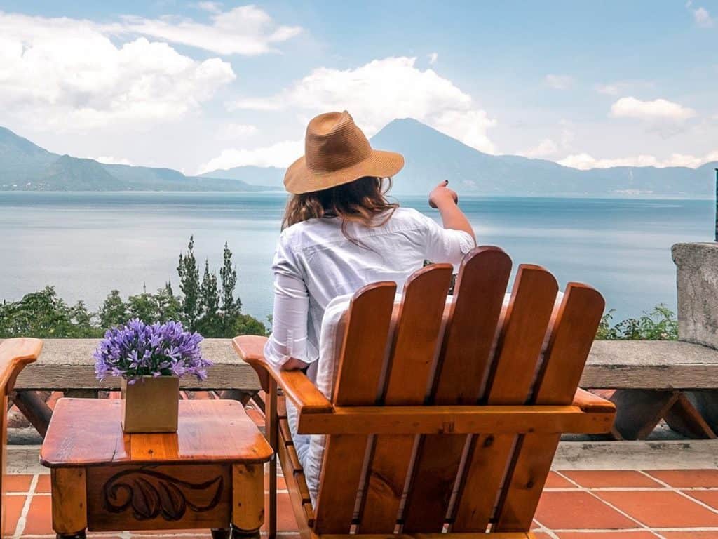 Relaxing woman enjoying a lakeside view with mountains in the background, sitting on a wooden chair.