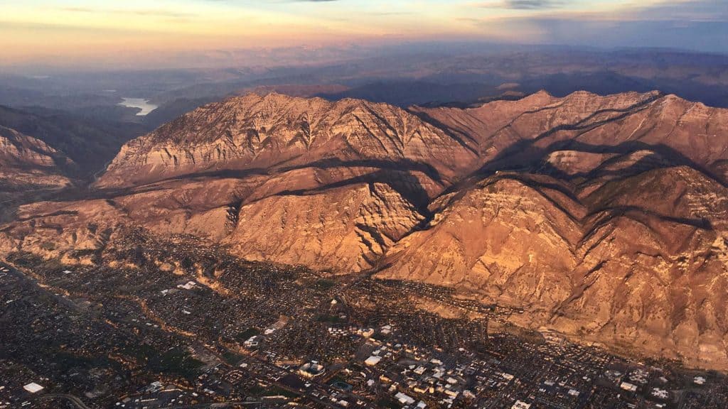 Mountain landscape with cityscape below at sunset, showcasing rugged terrain and scenic views.