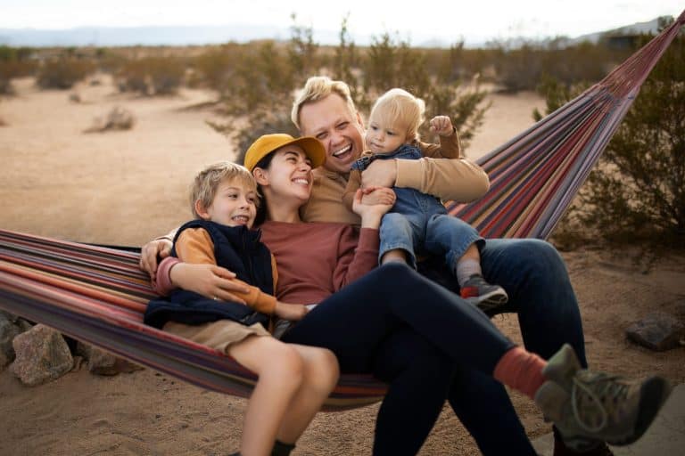 Family relaxing in a hammock in a desert landscape, smiling and playing with children.