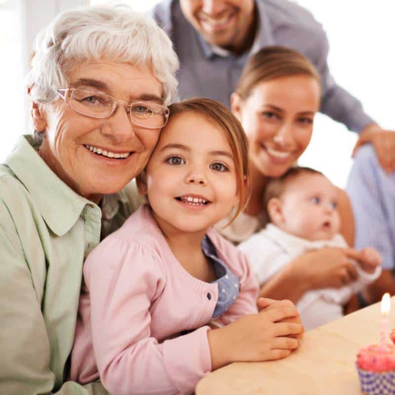 A smiling elderly woman with a young girl and family celebrating a birthday with a cake.