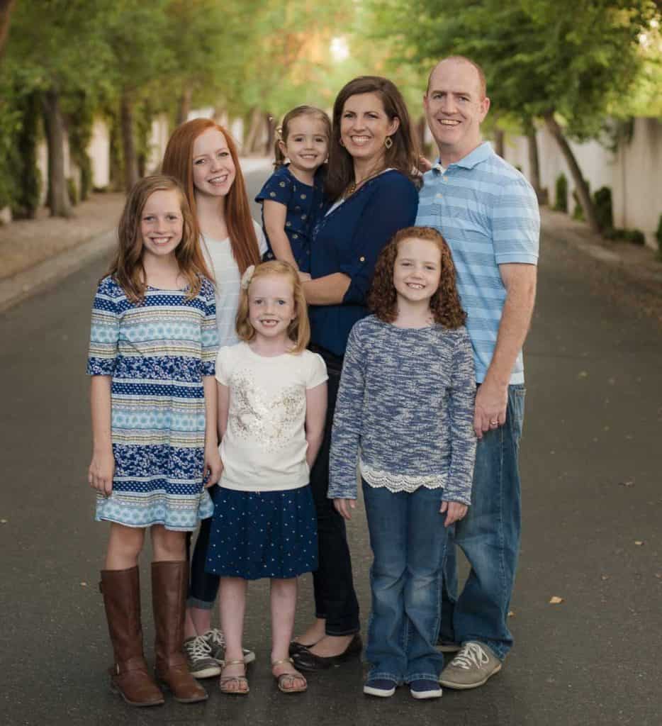 Family portrait of parents with four children outdoors in a park setting.