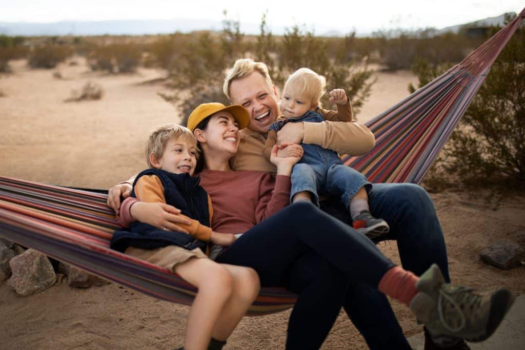 Family relaxing in a hammock in a desert landscape, smiling and playing with children.