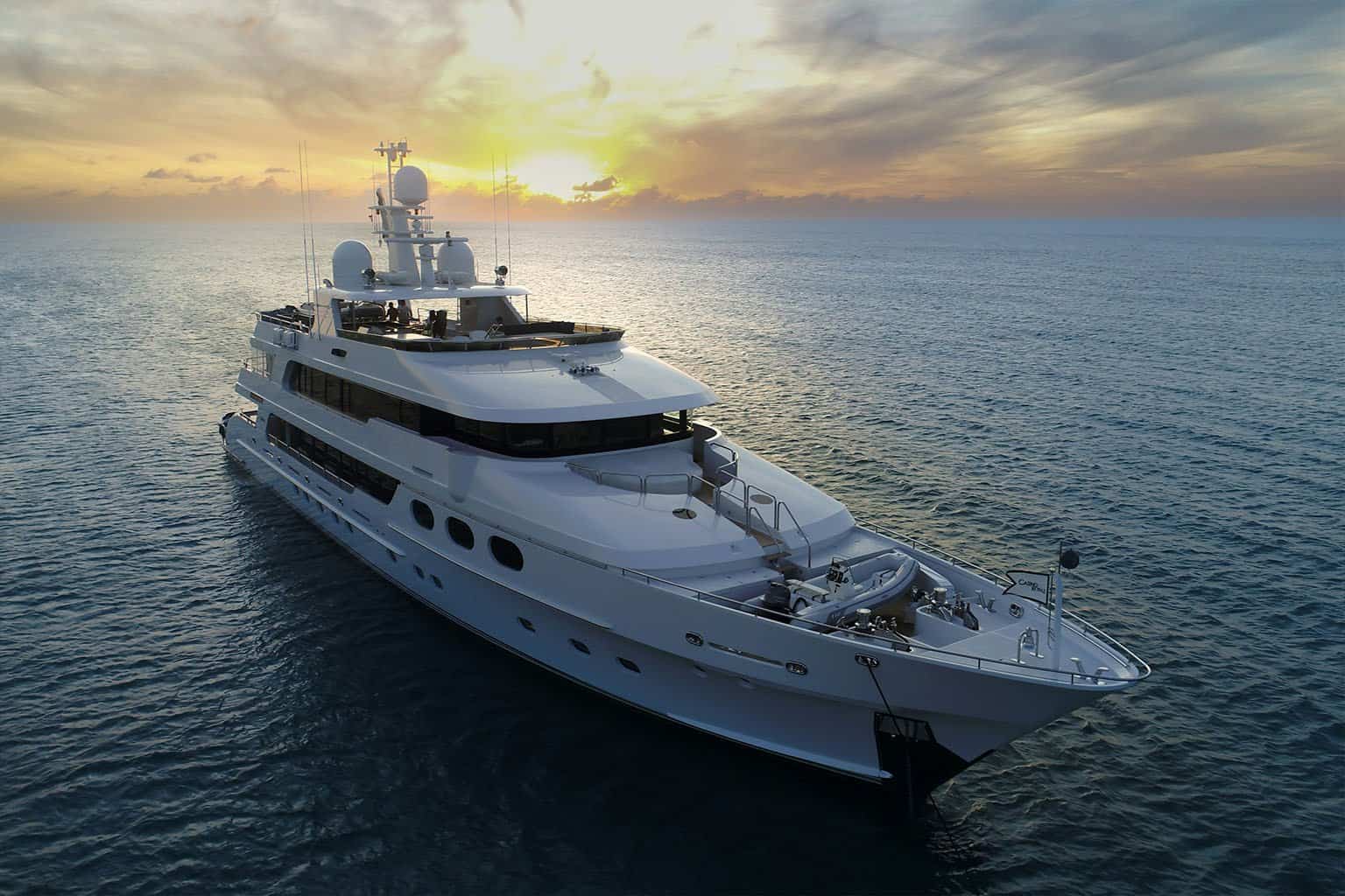 Luxury yacht sailing at sunset in open water, showcasing high-end maritime lifestyle.