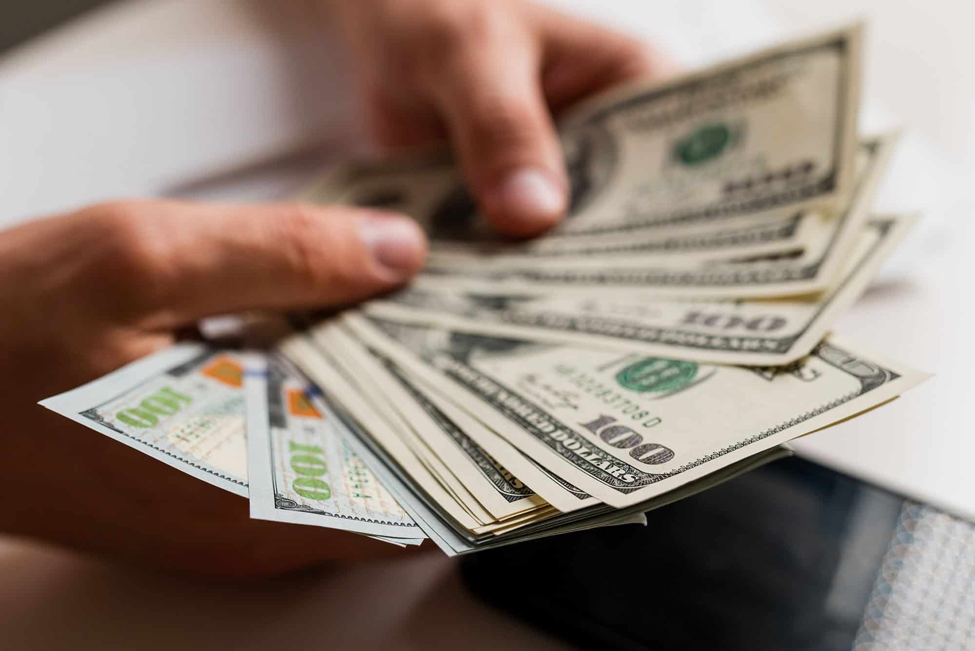 Hands holding a stack of US dollar bills, cash payout concept.