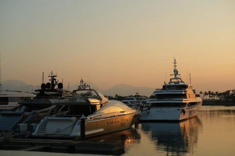 Luxury yachts moored at marina with calm water and sunset sky.
